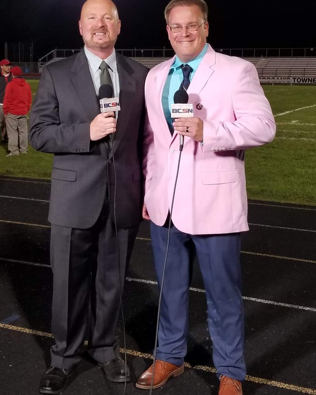 Tim Clagg in a pink jacket with his BCSN broadcast partner on the track before a Friday night football game